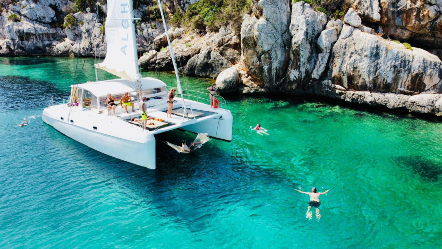 Escursionisti fanno il bagno durante l'escursione in catamarano nella baia di Porto Conte