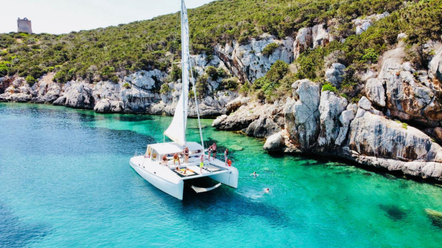 Il catamarano sosta e gli escursionisti fanno il bagno nell'acqua cristallina del Parco di Porto Conte