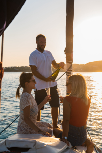Skipper schenkt zwei Mädchen beim Aperitif auf einem Segelboot in Stintino Weißwein ein