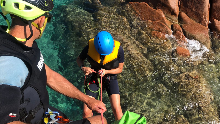 Boy with equipment makes a guided rope climb in the blue sea of central east Sardinia