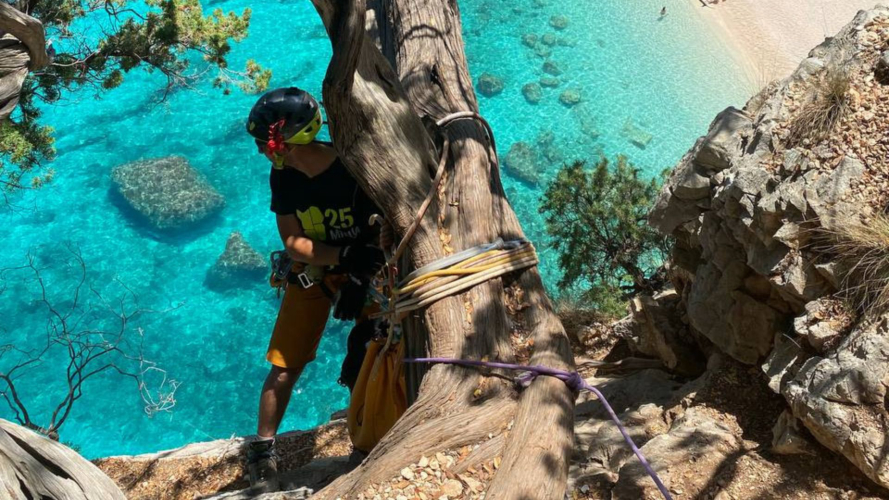 Senderista durante un rápel con cuerda con el mar turquesa del Golfo de Orosei a sus espaldas