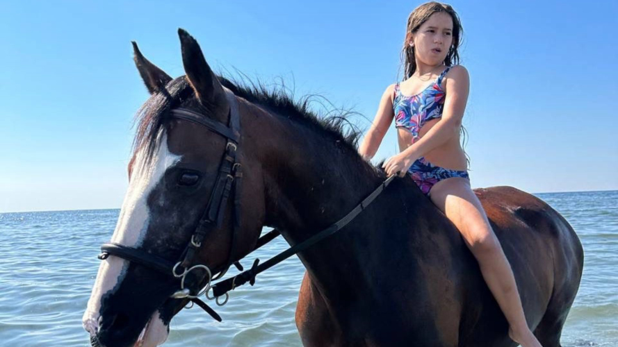Kind auf dem Pferderücken bei einem Strandspaziergang in Cagliari