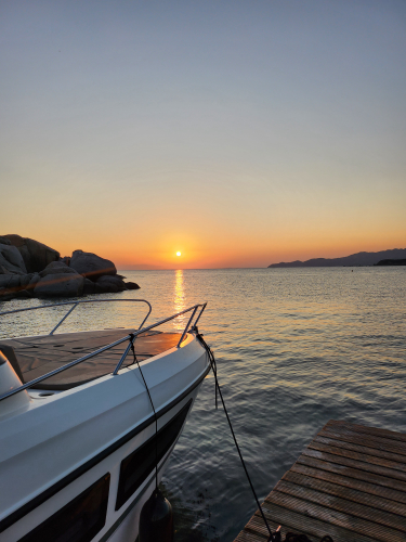 Mini yacht mentre naviga nelle acque cristalline di Punta Molentis al tramonto