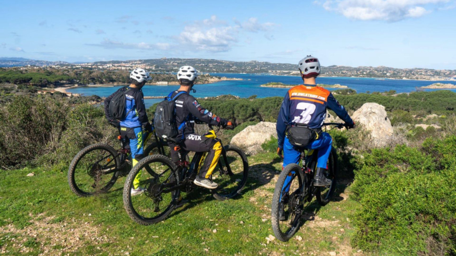 Trois jeunes hommes sur des vélos électriques se détendent en regardant la mer dans l'archipel de La Maddalena.