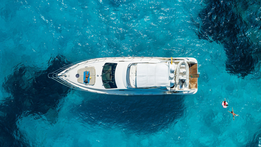 Immagine di un yacht di lusso con persone che nuotano e prendono il sole nel mare cristallino di Porto Cervo