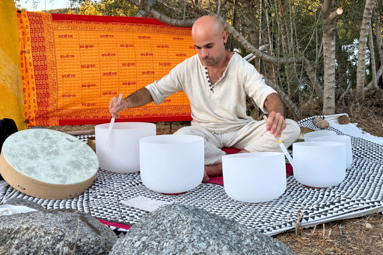 Un uomo suona strumenti di sound healing come gong, campane di cristallo e tamburi terapeutici in un ambiente tranquillo vicino al verde e a siti archeologici.