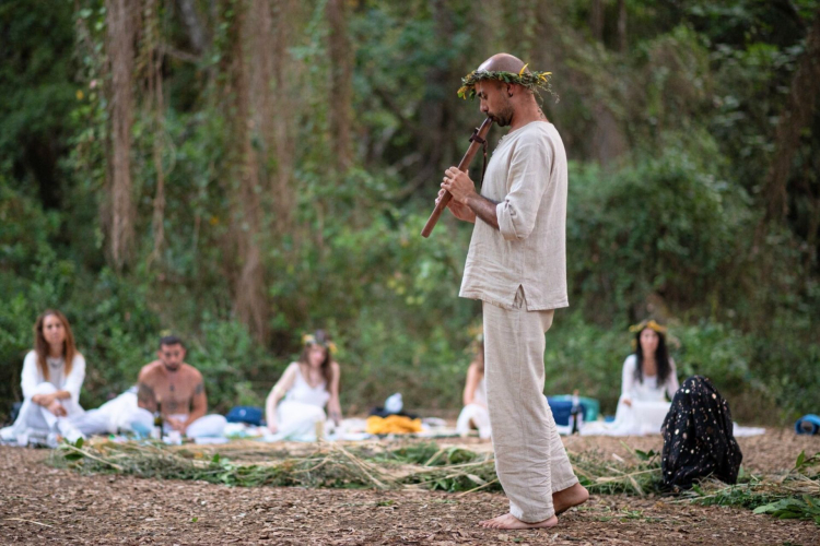 Un uomo suona uno strumento musicale in un ambiente naturale, circondato da persone in meditazione.