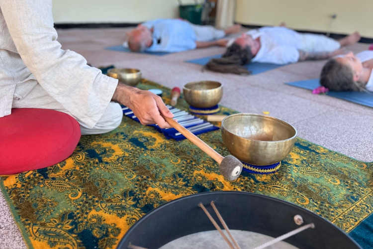 Persone sdraiate su tappetini in una stanza con strumenti musicali per una sessione di sound healing.