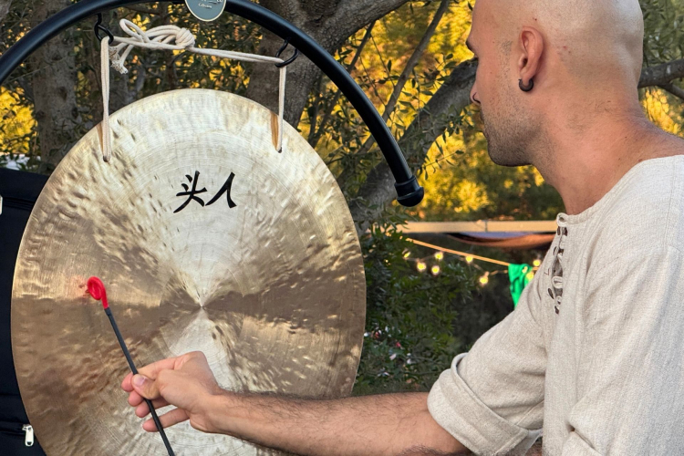 Uomo che suona un gong con un martelletto, in un ambiente tranquillo e verdeggiante.