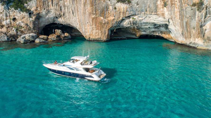 Un bateau de luxe navigue dans les eaux cristallines de la côte de Baunei avec une grotte naturelle visible