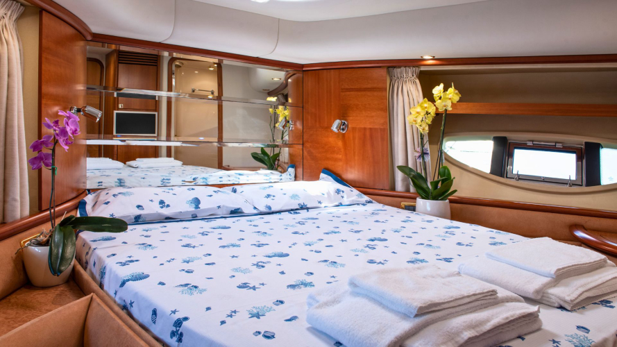 Une chambre sur un yacht de luxe avec des lits bien faits, des fleurs et une vue sur la mer à travers une fenêtre panoramique.