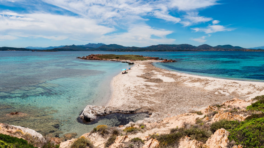 Un gommone naviga lungo una costa sarda con spiagge bianche e acque cristalline