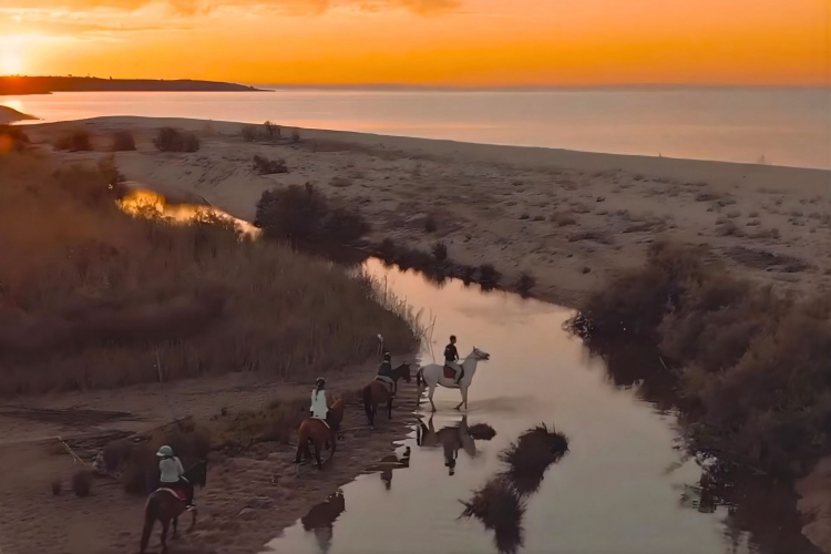 Persone a cavallo sulla spiaggia di Orosei al sorgere del sole, vicino alla foce di un fiume