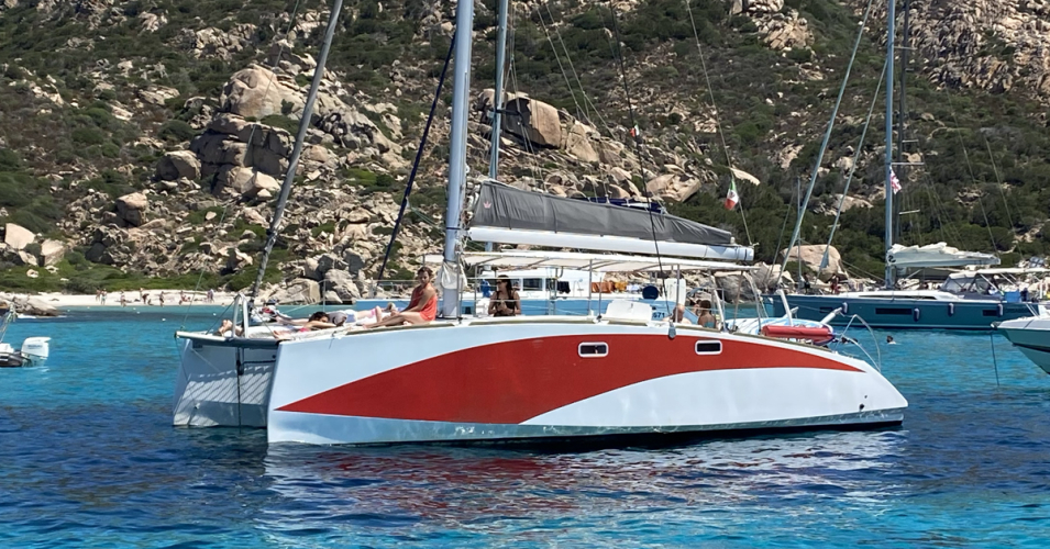 Catamarán con personas a bordo en aguas cristalinas frente a una isla rocosa