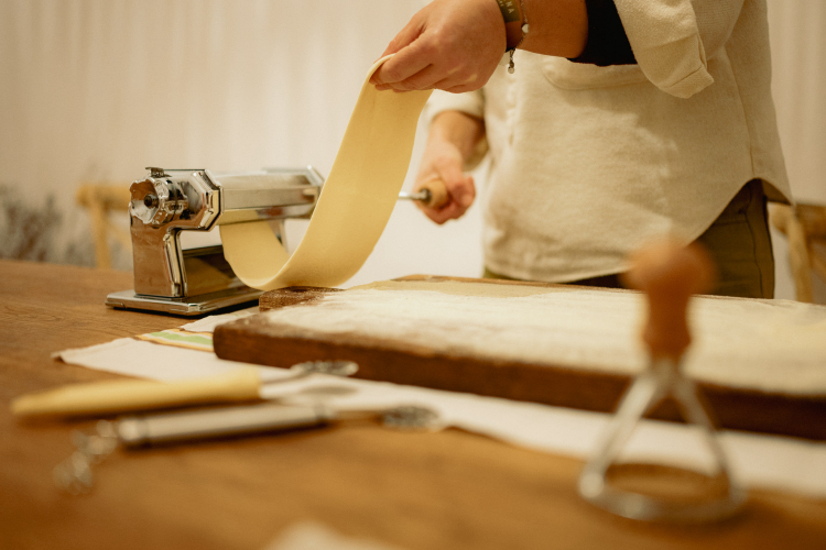 Una persona utilizza una macchina per la pasta per creare ravioli fatti in casa su un tavolo con altri utensili da cucina