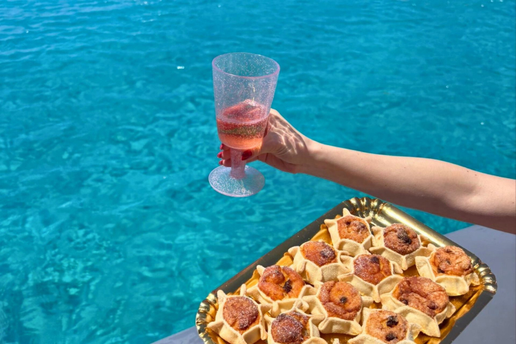 Snack an Bord mit einem Glas Rosé und typisch sardischen Desserts inmitten des türkisfarbenen Meeres