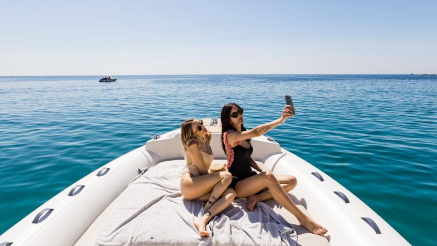 Due donne in costume da bagno su un gommone, una con uno smartphone in mano a Villasimius