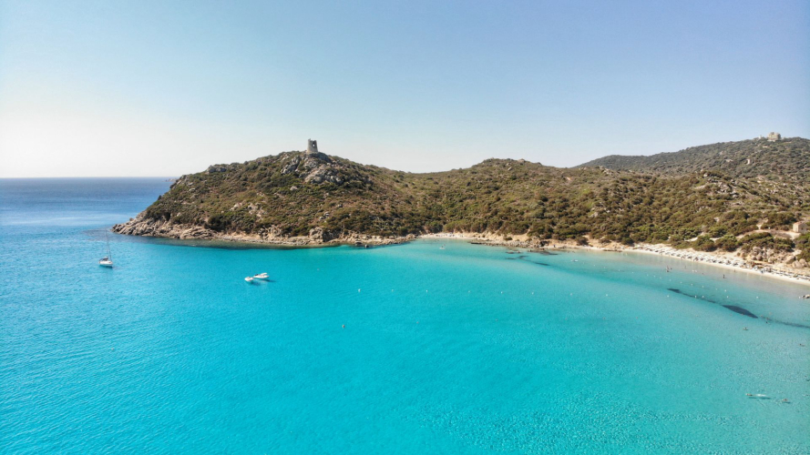 Immagine di una spiaggia con acqua cristallina con la torre di Porto Giunco