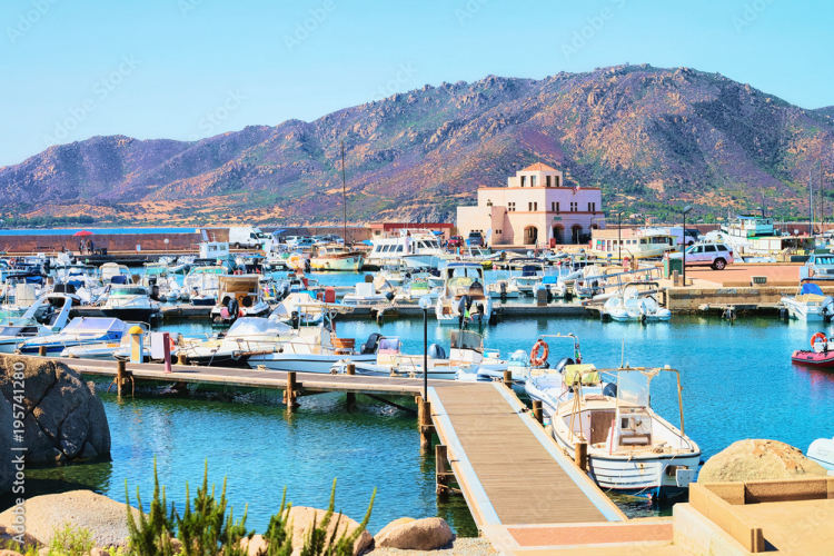 Immagine di un porto Marina di Villasimius con barche ormeggiate e una struttura in lontananza, con montagne sullo sfondo