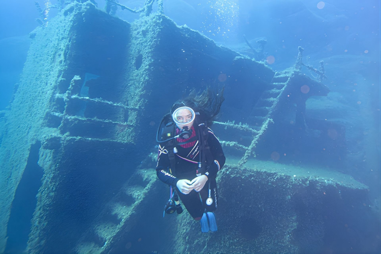 Una ragazza in immersione guidata con attrezzatura completa esplora un relitto sommerso