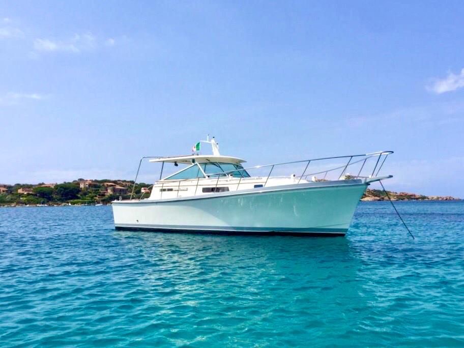 Un barco a motor navega entre las islas del archipiélago de La Maddalena, con una costa de fondo