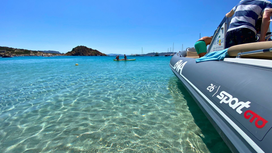 Un bateau à moteur navigue dans les eaux turquoises avec des îles en arrière-plan et des gens dans l'eau