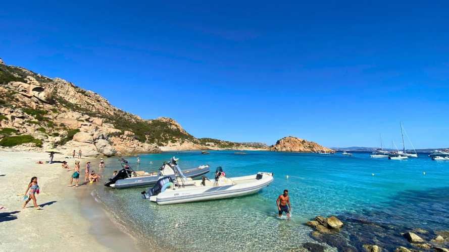 Les gens profitent d'une plage avec des bateaux amarrés, des eaux turquoises et des montagnes en arrière-plan