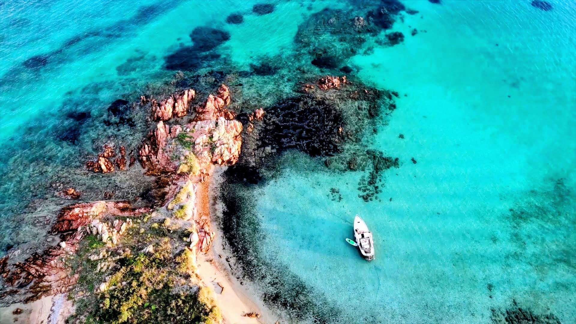 Image of a gozzo moored in crystal clear waters with rocks and a visible coastline