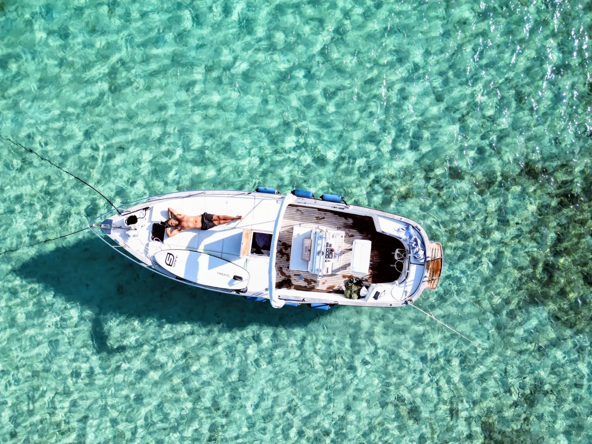 Image of a gozzo with a man lying on board in crystal clear waters, near an island with vegetation