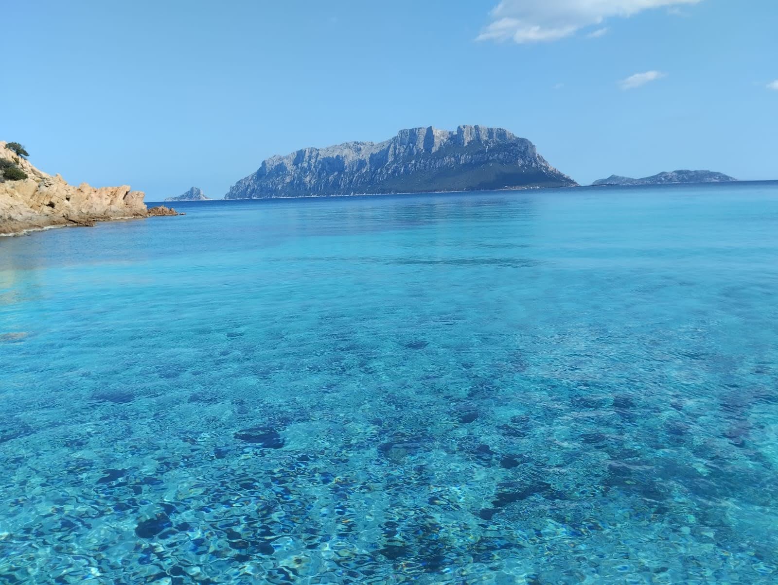 Image of a crystal clear sea with an island in the background and rocky cliffs