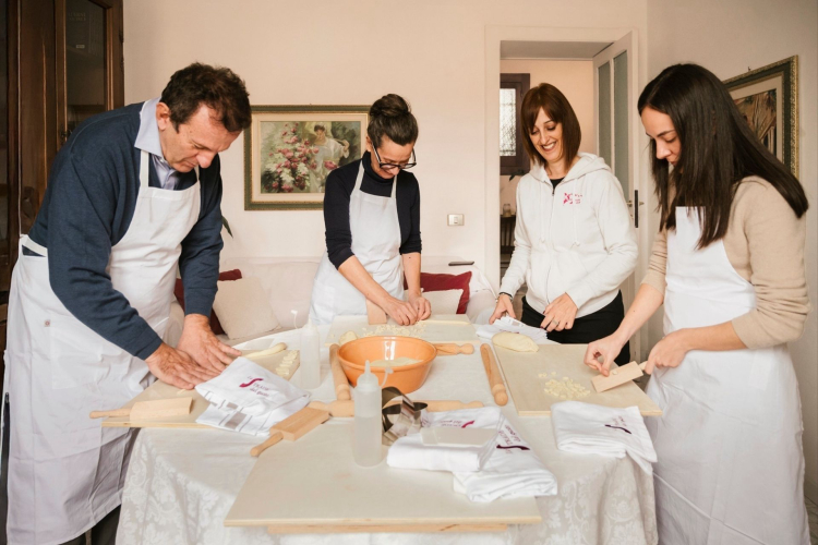 Grupo de personas en una cocina preparando pasta típica de Cerdeña, con varios utensilios e ingredientes sobre la mesa.