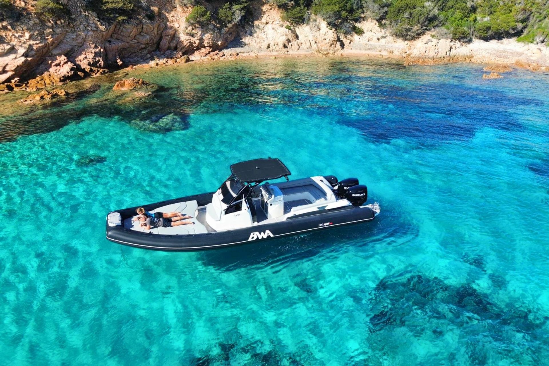 Ein Beiboot segelt mit zwei Personen an Bord beim Sonnenbaden durch das kristallklare Wasser des La Maddalena-Archipels