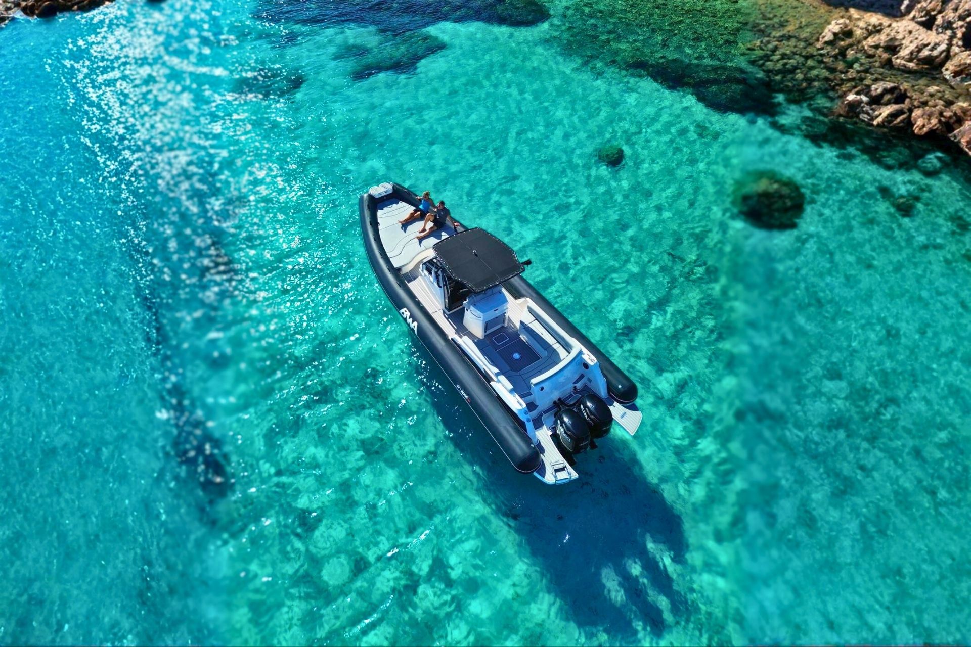 Ein Beiboot segelt durch das kristallklare Wasser des La Maddalena-Archipels, an Bord sitzen zwei Personen.