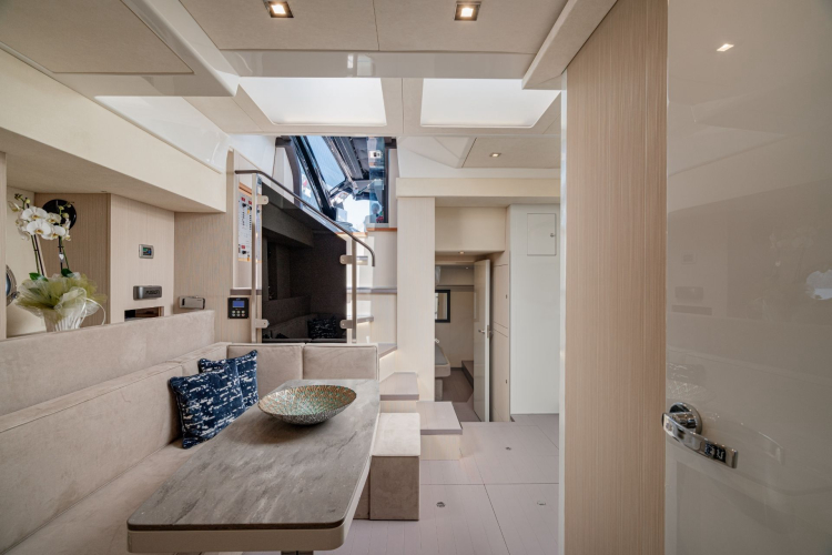 Innenraum einer luxuriösen Privatyacht mit Tisch, Sofa, Blumen und natürlichem Licht durch Dachfenster.