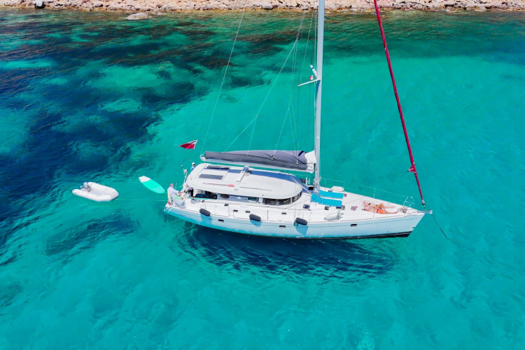 Un monomarano a vela naviga in acque cristalline con persone a bordo