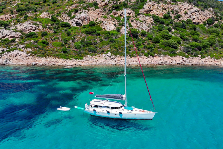 Un monomarano a vela naviga in acque cristalline davanti a un'isola rocciosa
