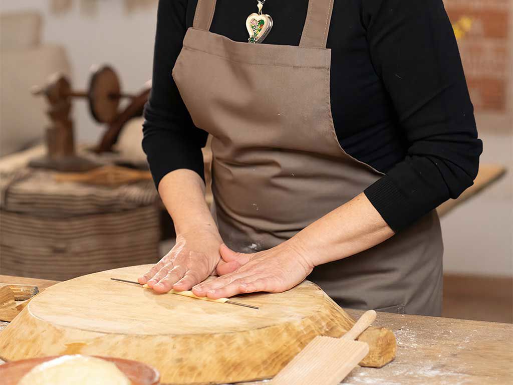 Una persona en un taller de cocina que está trabajando en un trozo de pasta fresca en una tabla de cortar de madera
