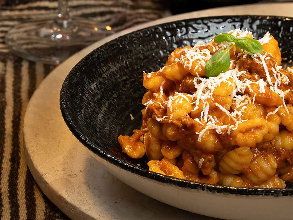 Un plato de pasta fresca servido en un elegante bol negro con una pizca de queso