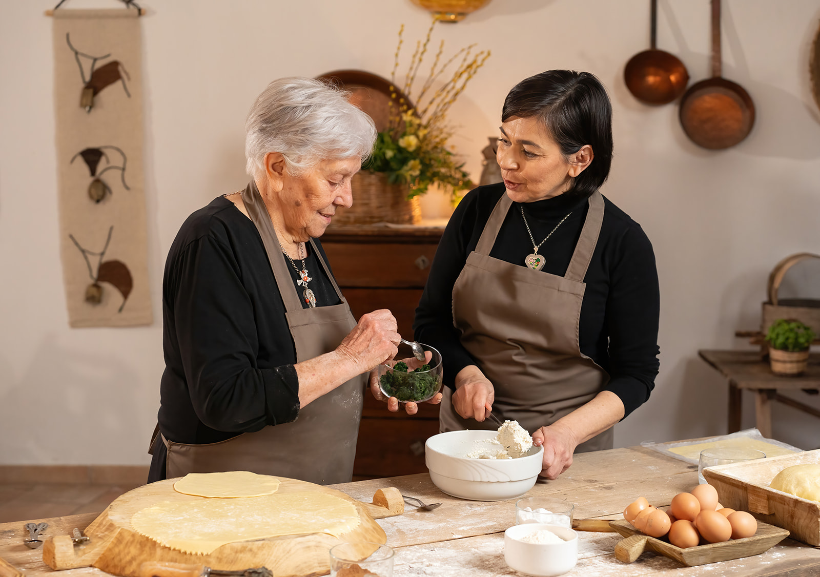 Dos mujeres en la cocina, una mayor enseñando a la más pequeña a preparar pasta fresca