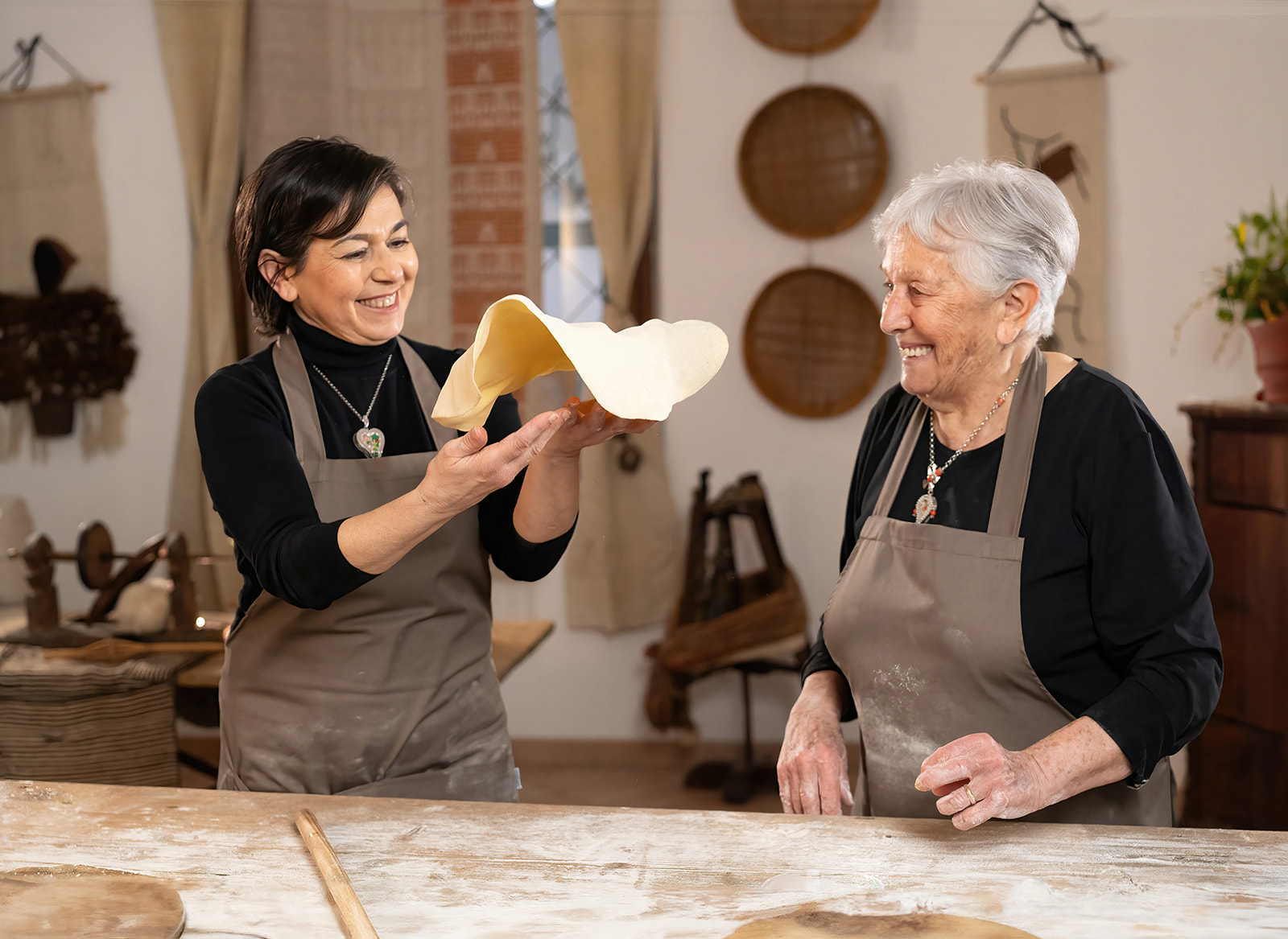 Dos mujeres en un taller de pasta fresca, una sostiene un trozo de pasta fresca recién enrollado
