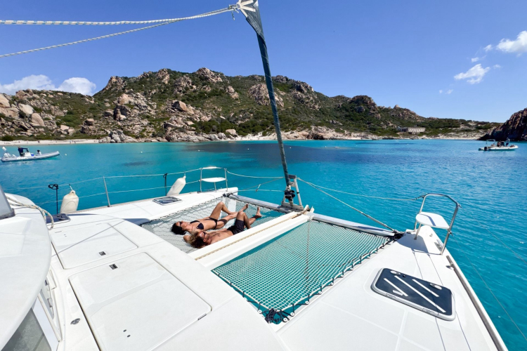 Deux personnes se détendent sur un catamaran dans une mer turquoise avec des îles en arrière-plan.