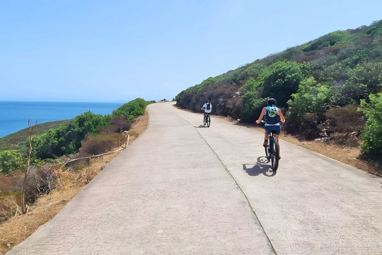 Two people riding electric bikes along a coastal path with a view of the sea and the surrounding nature
