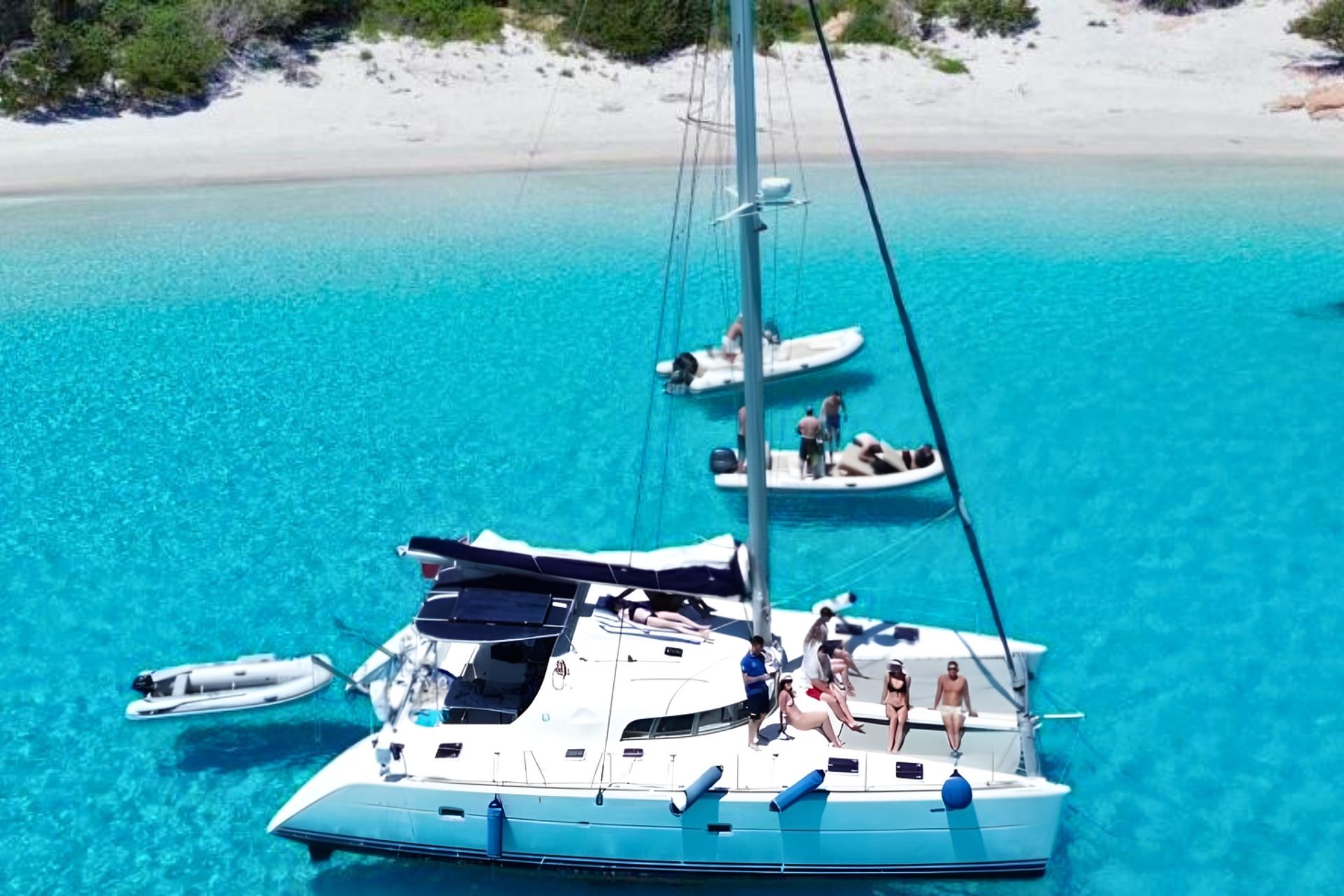Catamarán con personas a bordo y un entorno con playa y mar cristalino.
