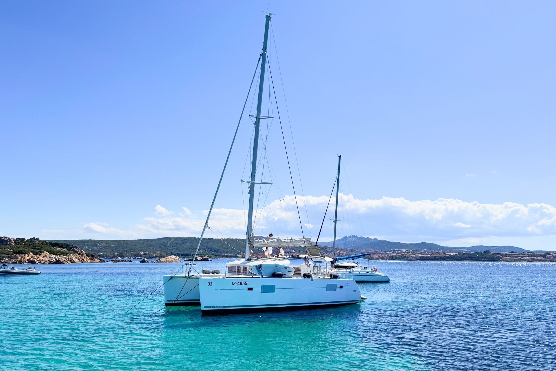 Un catamarán blanco navega en aguas cristalinas de color azul turquesa, con montañas de fondo.