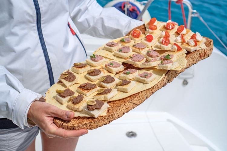 Person holding a plate with various appetizers on a wooden board on a sailboat.