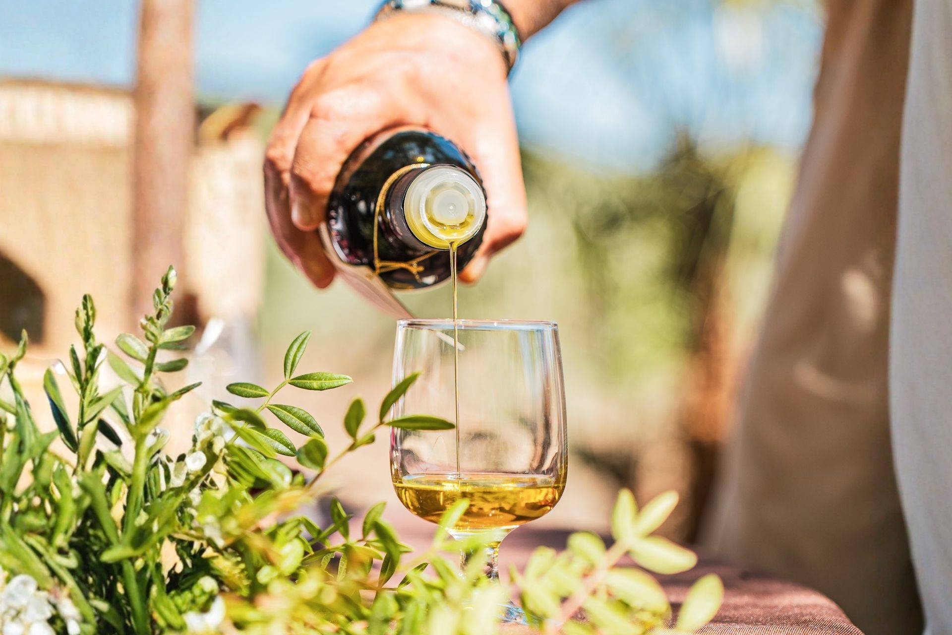 Una persona vierte aceite en un vaso entre plantas y flores verdes.