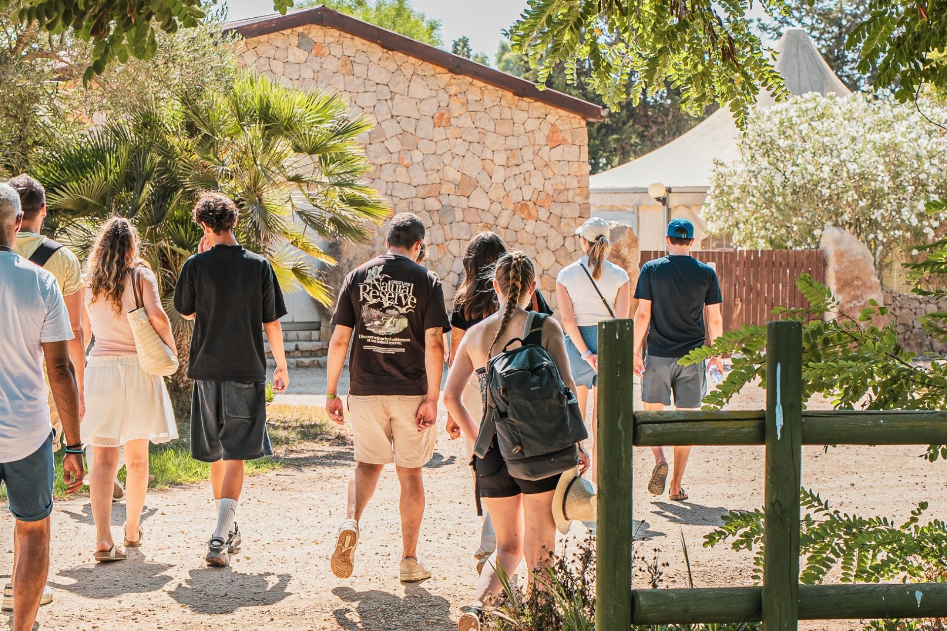 Un grupo de personas camina por un sendero entre árboles y vegetación, tal vez para hacer un recorrido gastronómico y vinícola en un olivar.