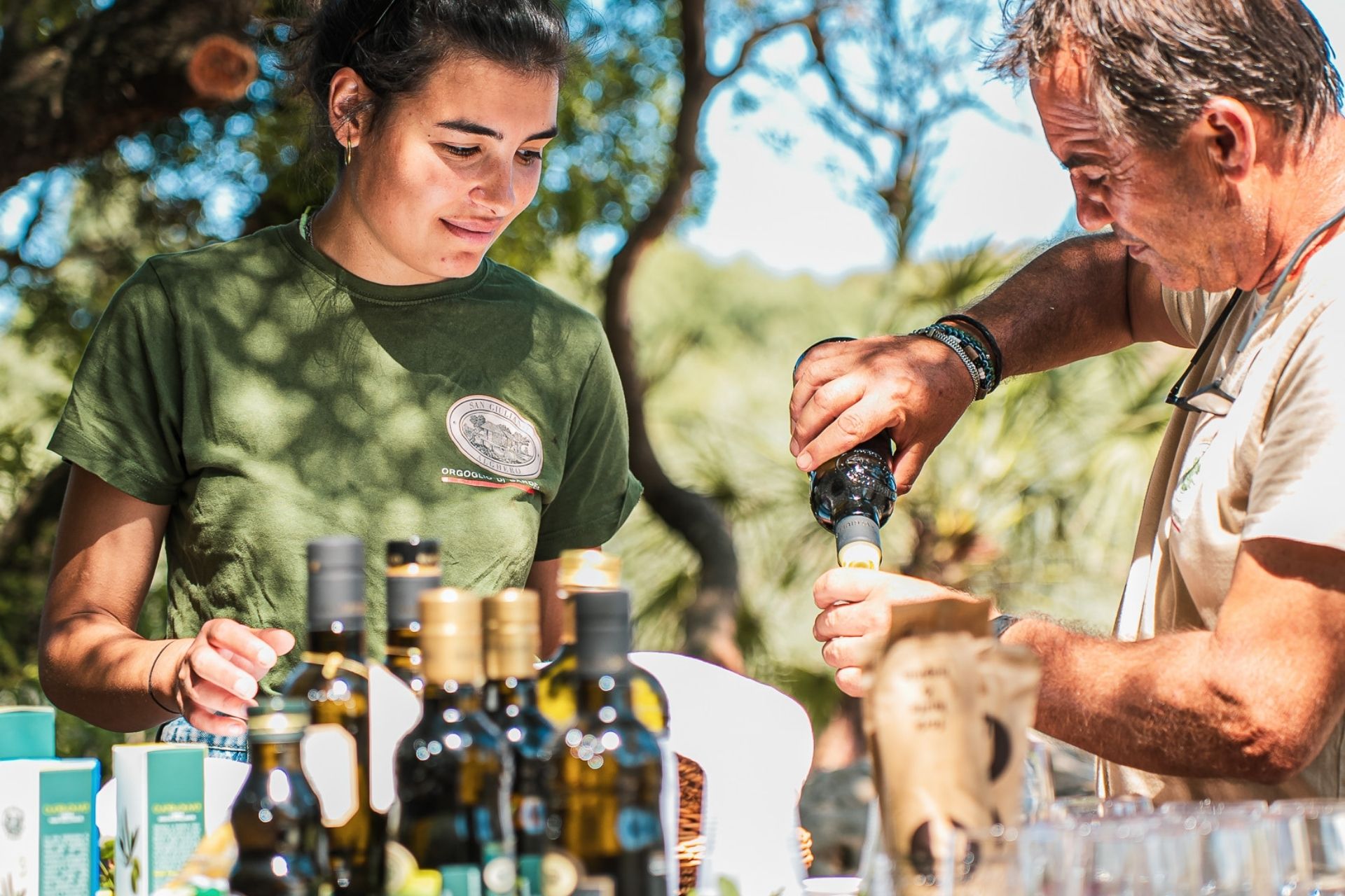 Una mujer y un hombre prueban aceites embotellados en un olivar centenario de Alghero.