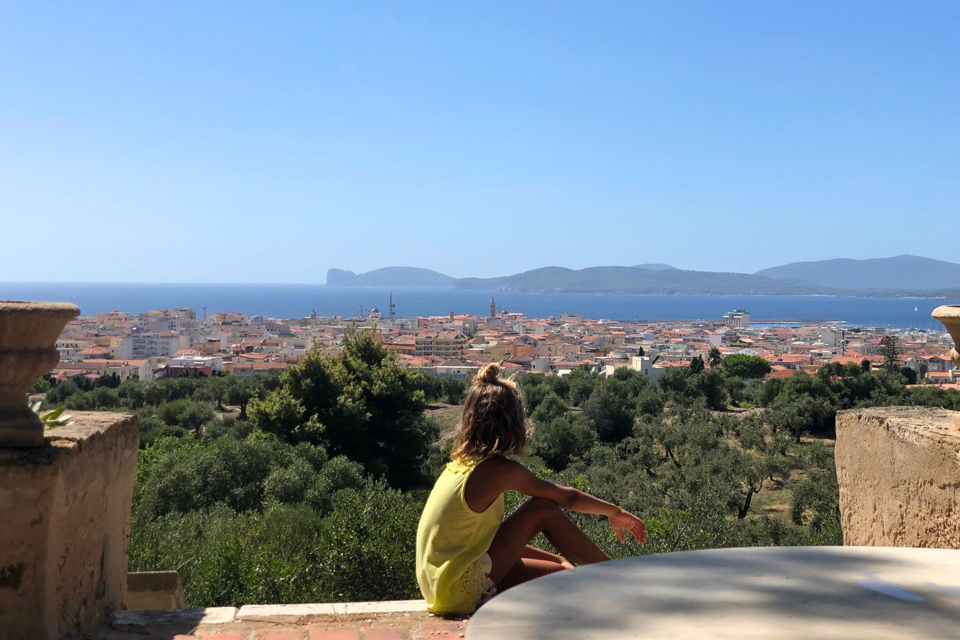 A girl sitting on the panoramic terrace overlooking the sea and the city of Alghero.