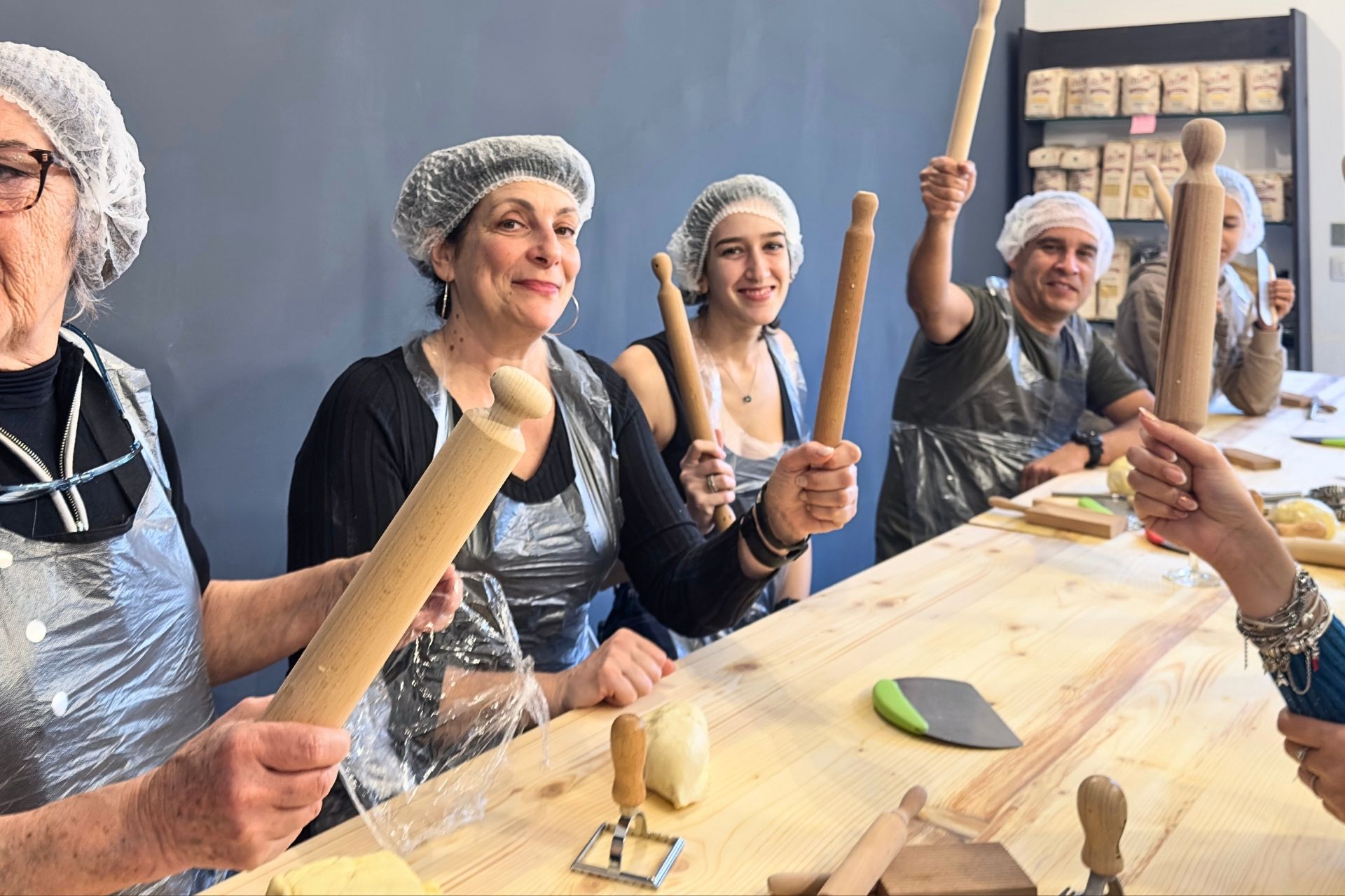 Un gruppo di persone con grembiuli e cuffie in un laboratorio di pasta fresca ad Alghero, Sardegna, con strumenti da cucina.